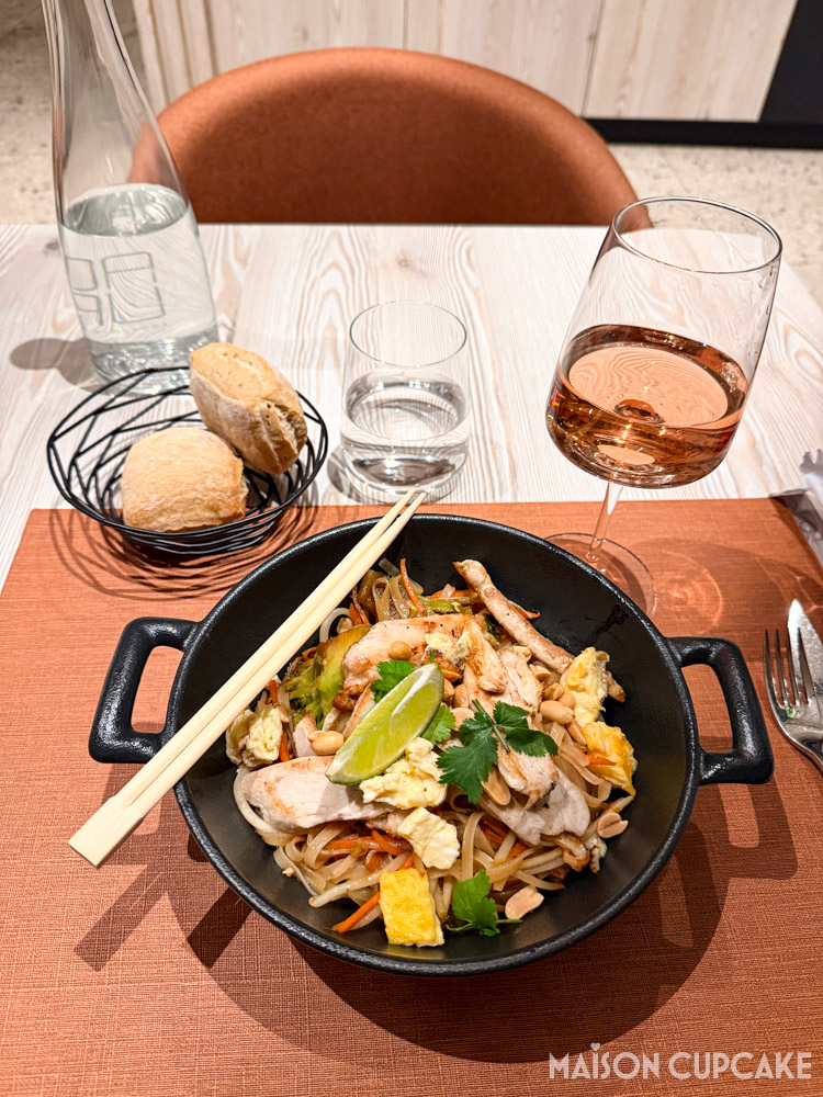 Pad Thai in black bowl with chopsticks, a glass of rosé wine and bread rolls at Novotel hotel restaurant.