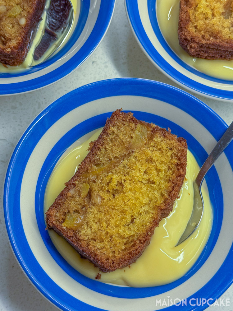 Thick slice of Apple and Pine Nut Pound Cake in Cornish Blue bowl with spoon in yellow custard - overhead portrait view