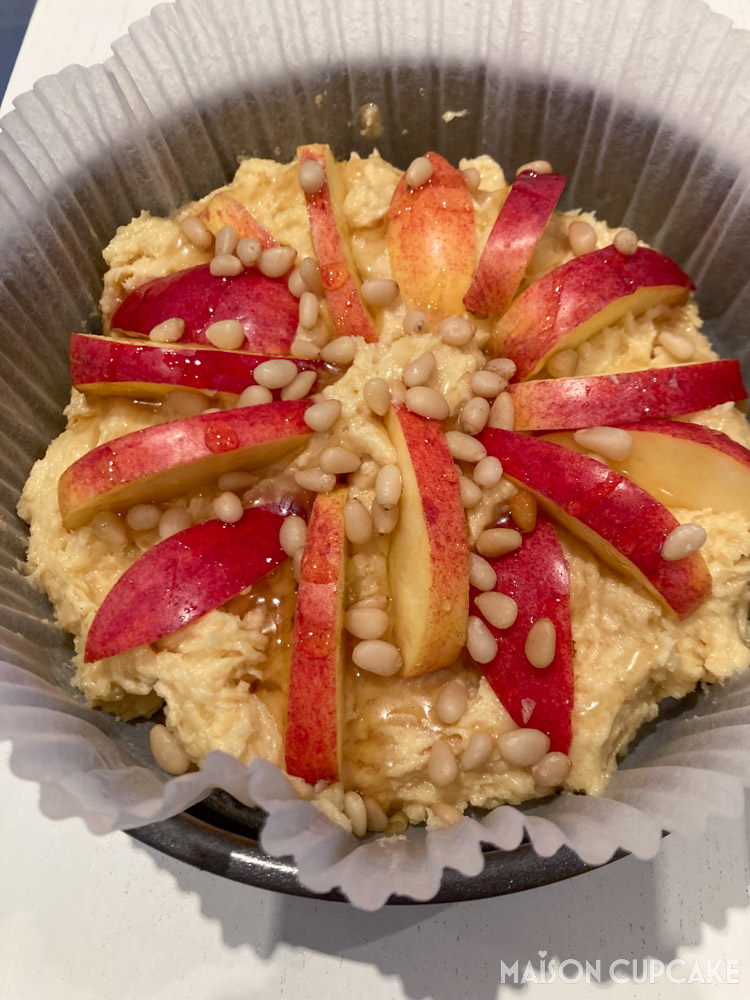 Overhead image of apple and pine nut pound cake batter in lined round tin before baking showing red apple slices
