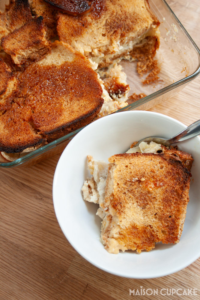 Overhead portrait shot of Banoffee Bread and Butter pudding, portion in white bowl with spoon below, larger oven dish above.