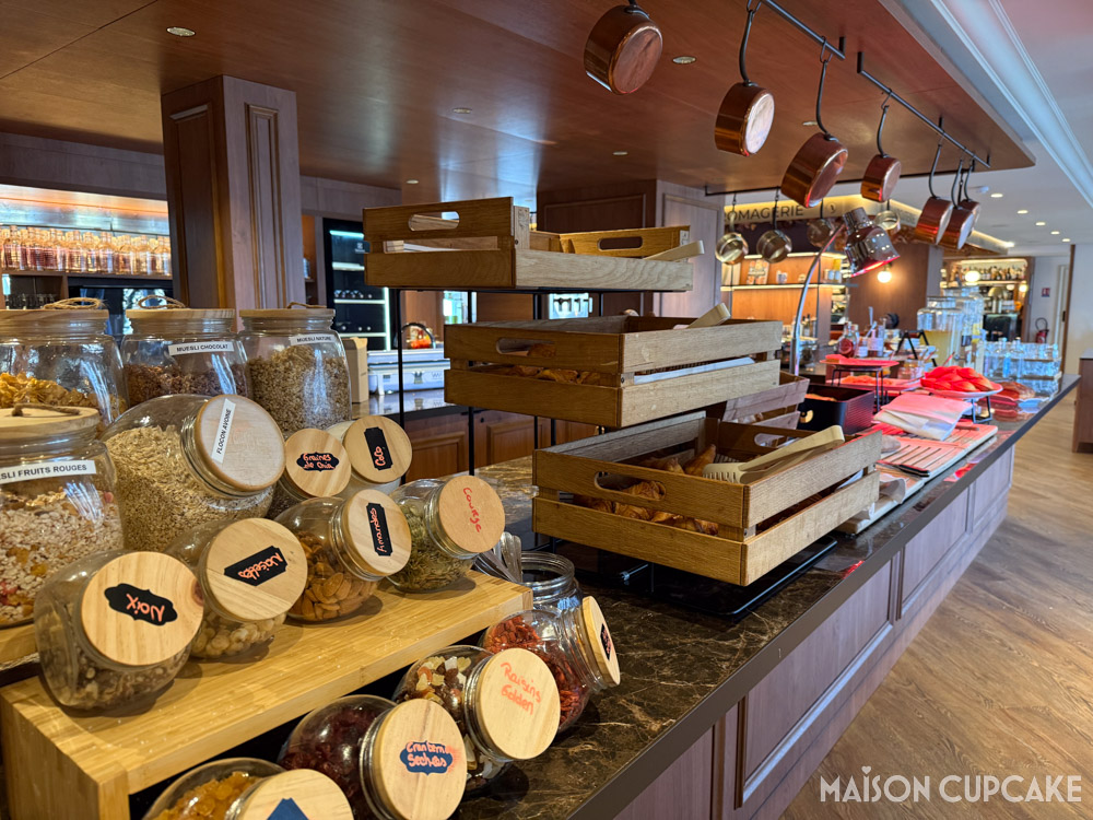 Breakfast buffet at hotel, a rack of glass cereal jars with wooden lids, copper saucepans dangle from above.