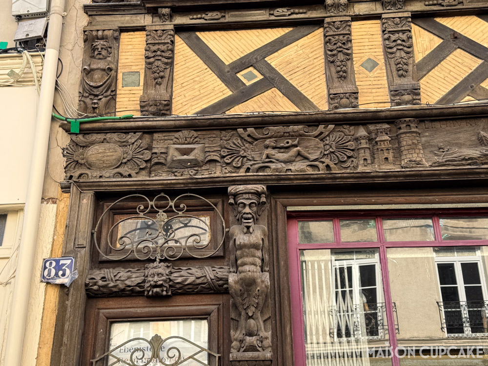 Details of mediaval building facade in Rouen, wooden carvings of figures and buildings, decorative ironwork and blue French door number.